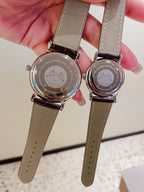 Pair of Longines watches with leather straps showing backs, engraved metal cases.