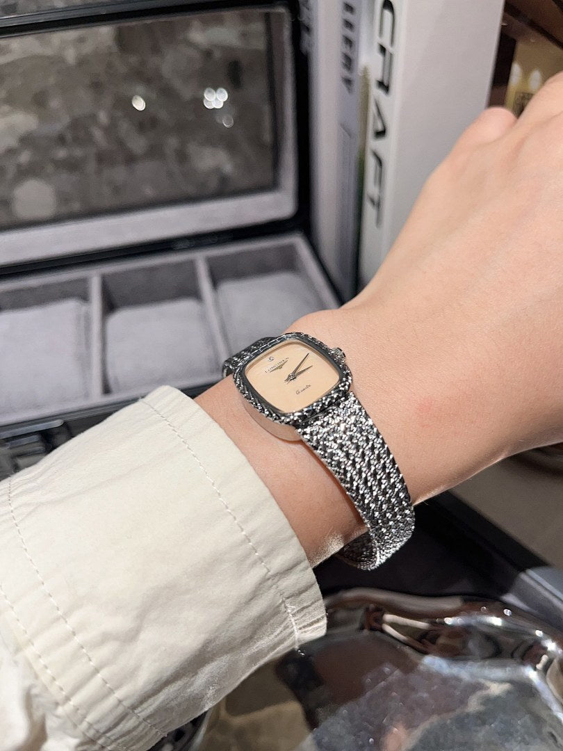 Square wristwatch with cream dial and silver mesh bracelet on wrist