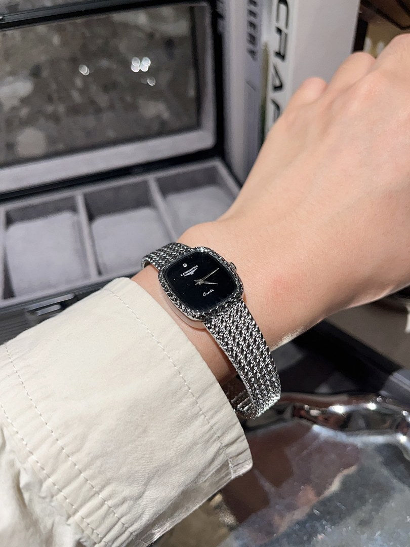 Square wristwatch with black dial and silver mesh bracelet on wrist