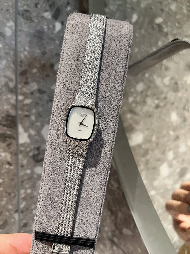 Square wristwatch with light dial and silver mesh strap, close-up on stand