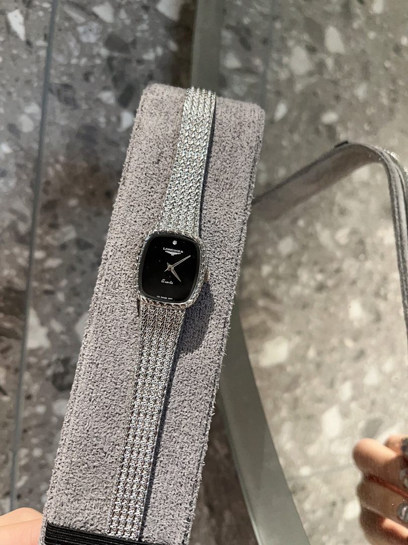 Square wristwatch with black dial and silver mesh strap, close-up