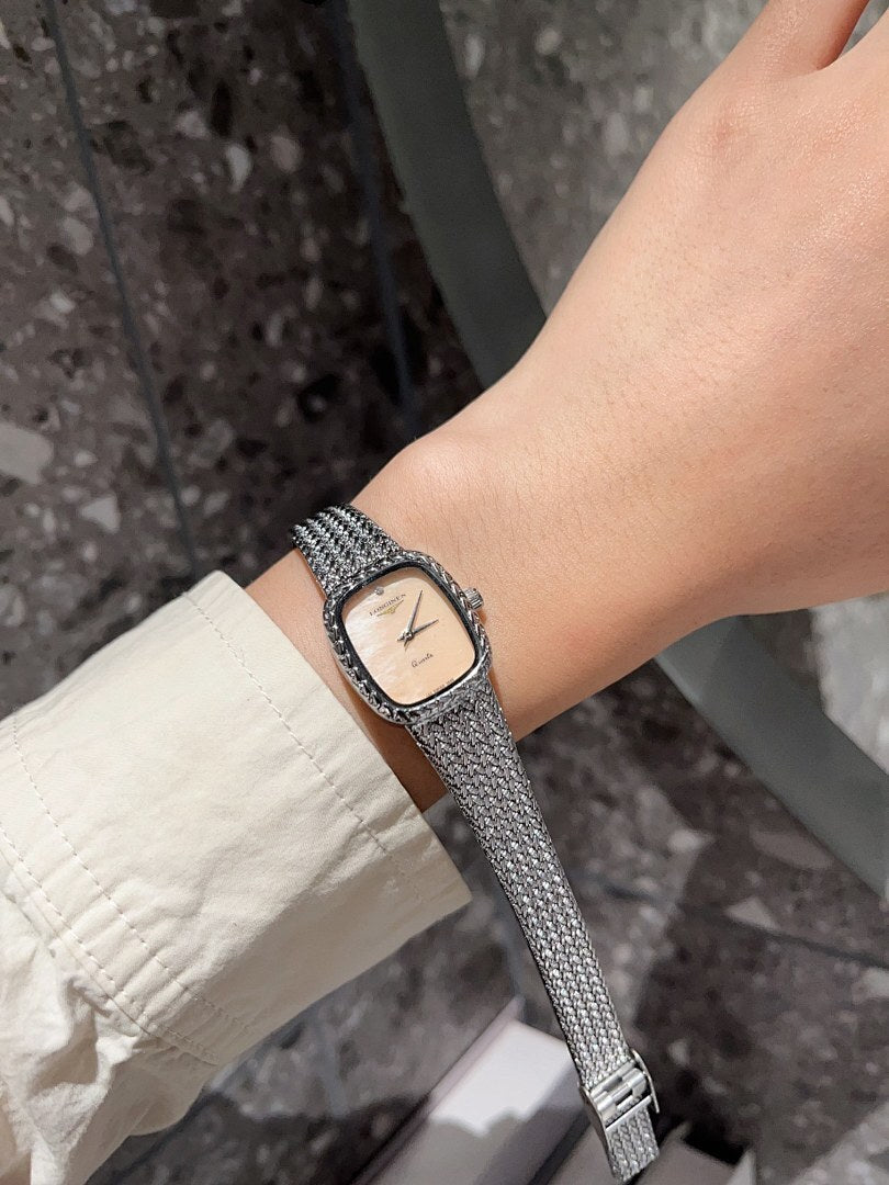 Square wristwatch with light dial and silver mesh bracelet on wrist