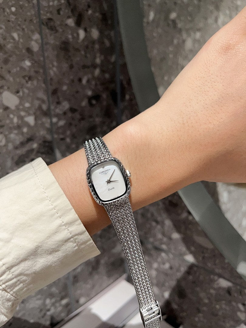Square wristwatch with white dial and silver mesh strap on wrist