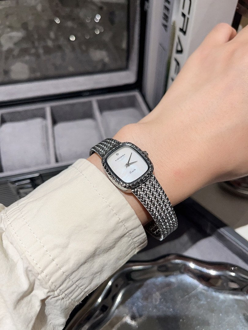 Square wristwatch with light dial and silver mesh bracelet on wrist
