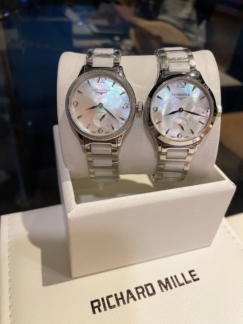 Longines stainless steel watch pair with silver bracelets and white dials on display