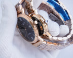 Rose-gold wristwatch with dark dial, metal link strap, and visible crown