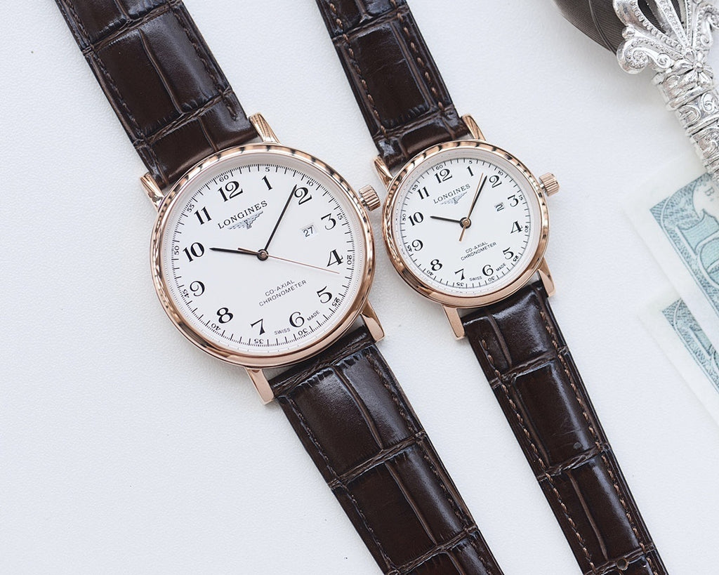 Longines watch pair with white dials, rose-gold cases, and brown leather straps on pillow