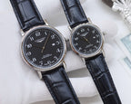 Longines watch pair with dark dials, stainless-steel cases, and black leather straps on pillow