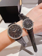 Leather-banded watch with dark dial, black strap; round silver-tone cases.
