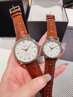 Leather-banded watch with white dial, brown strap; round silver-tone cases.