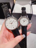 Leather-banded watch with white dial, black strap; two round silver-tone cases.