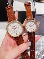 Leather-banded watch with white dial, brown strap; round gold-tone case.
