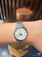 Longines wristwatch on an arm, silver metal bracelet and white dial with moon-phase subdial