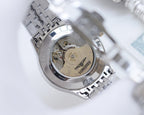 Wristwatch caseback with visible mechanical movement, silver metal finish.