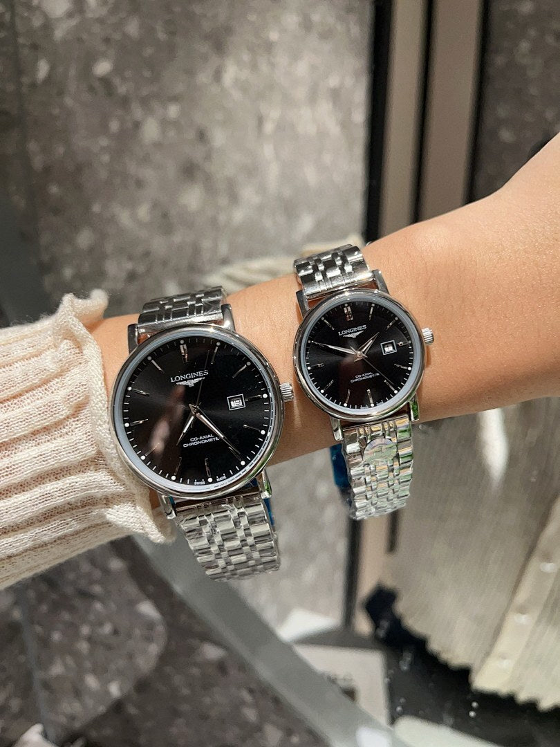 Two Longines watches with black dials and silver-toned metal link bracelets on wrist.