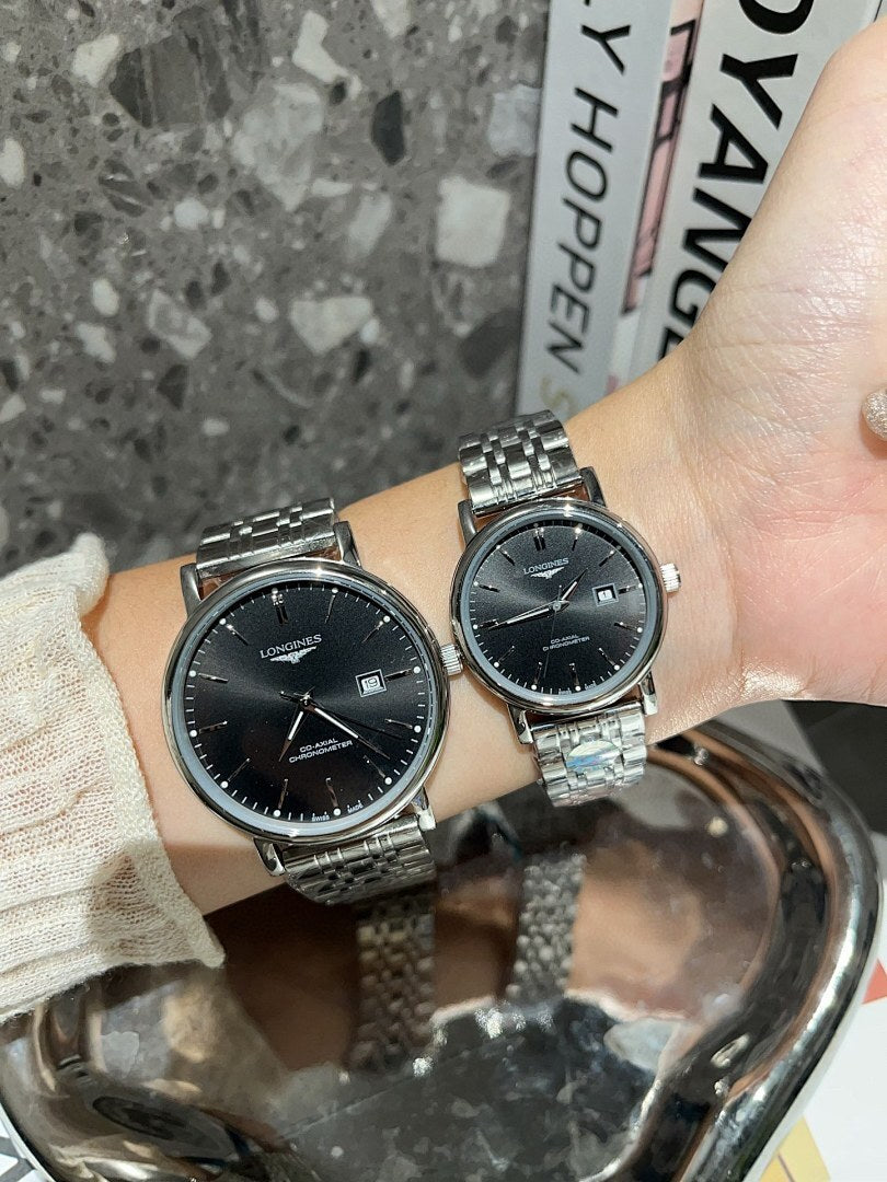 Two Longines watches with black dials and silver-toned metal link bracelets on wrist.