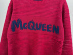 Magenta knit sweater close-up with large blue McQueen logo across the chest