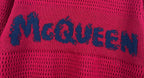Magenta knit sweater close-up with blue McQueen logo text across the fabric