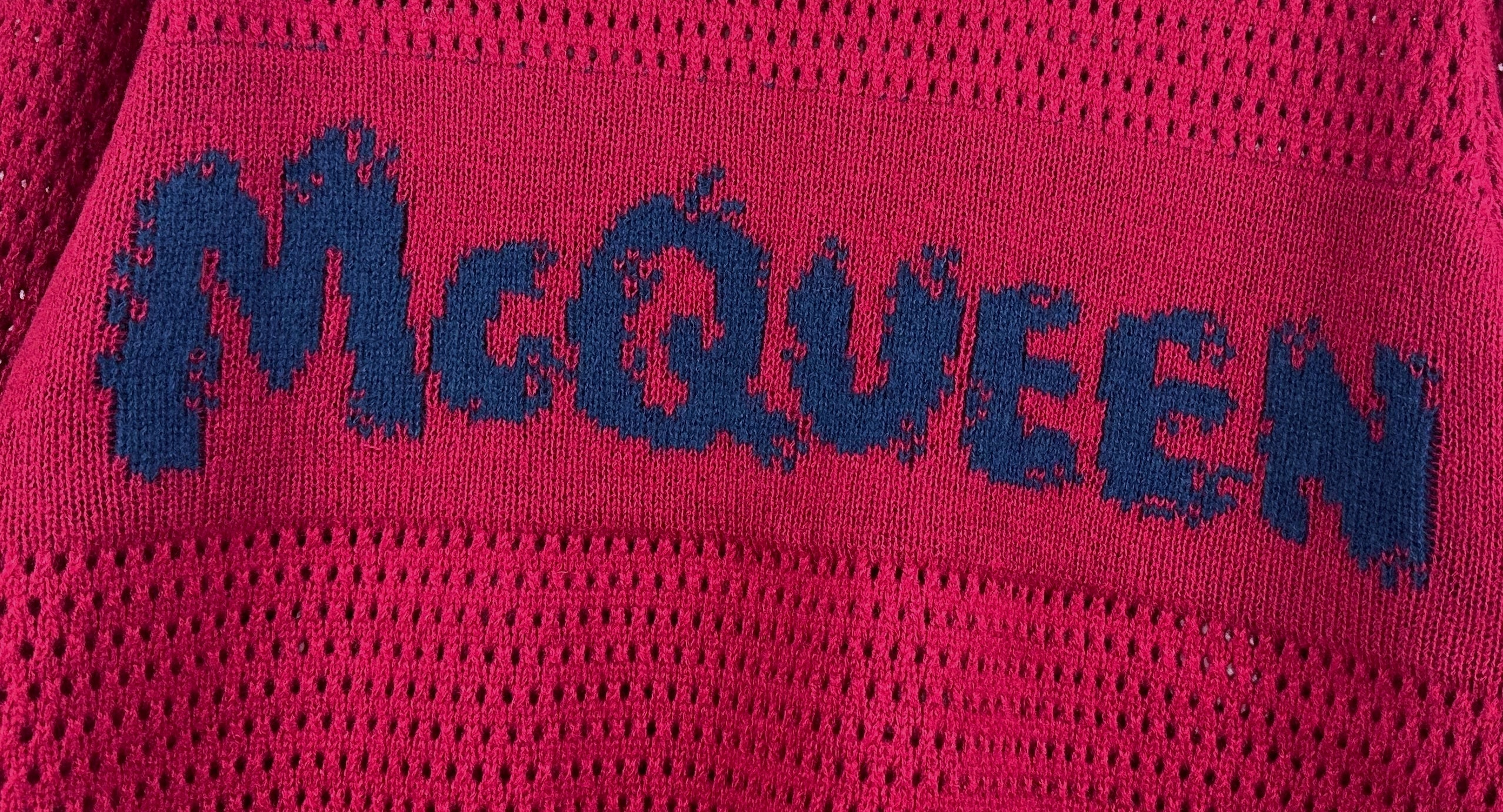 Magenta knit sweater close-up with blue McQueen logo text across the fabric