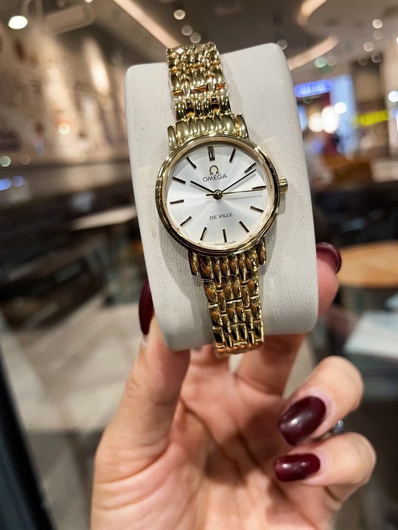 Omega wristwatch with gold-tone link bracelet and white dial on a display stand