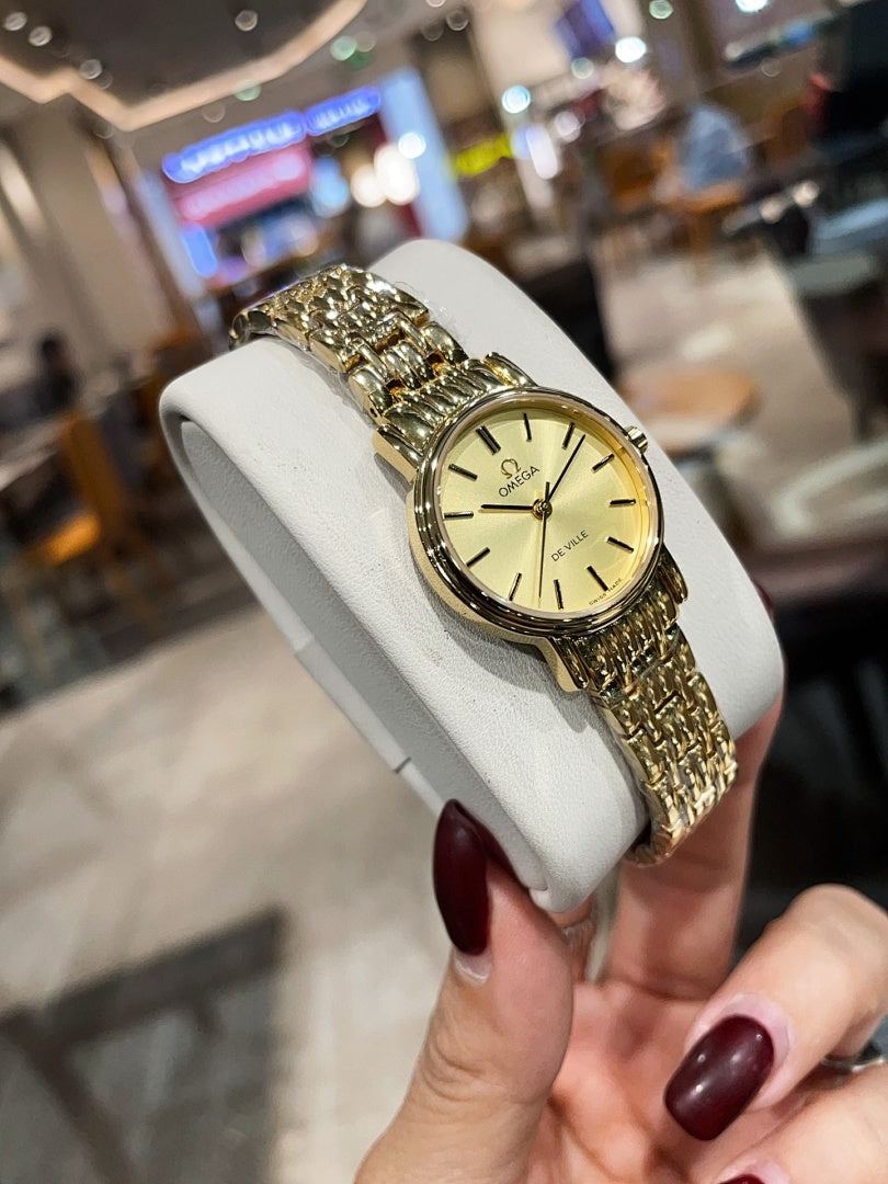 Omega wristwatch with gold-tone link bracelet and champagne dial, side view on stand