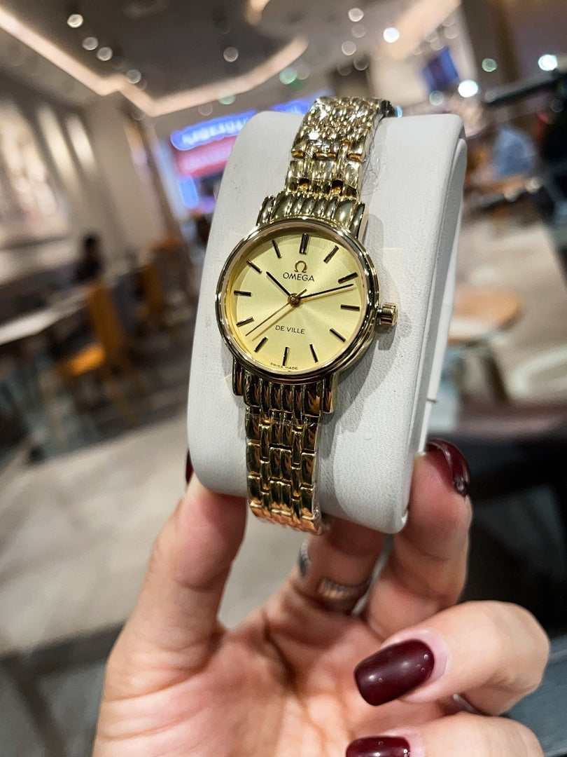 Omega wristwatch with gold-tone link bracelet and champagne dial, front view on stand