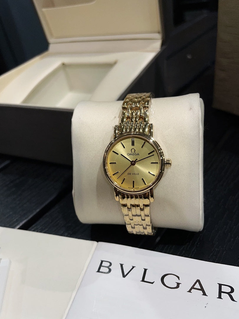Omega wristwatch with gold-tone bracelet and champagne dial on a white display stand