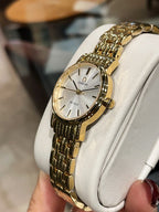 Omega wristwatch with gold-tone link bracelet and white dial, angled close-up on stand
