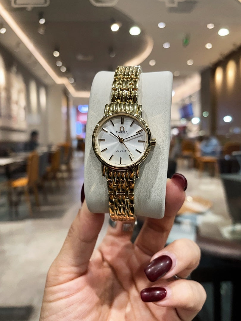 Omega wristwatch with gold-tone bracelet and white dial, front view on display stand