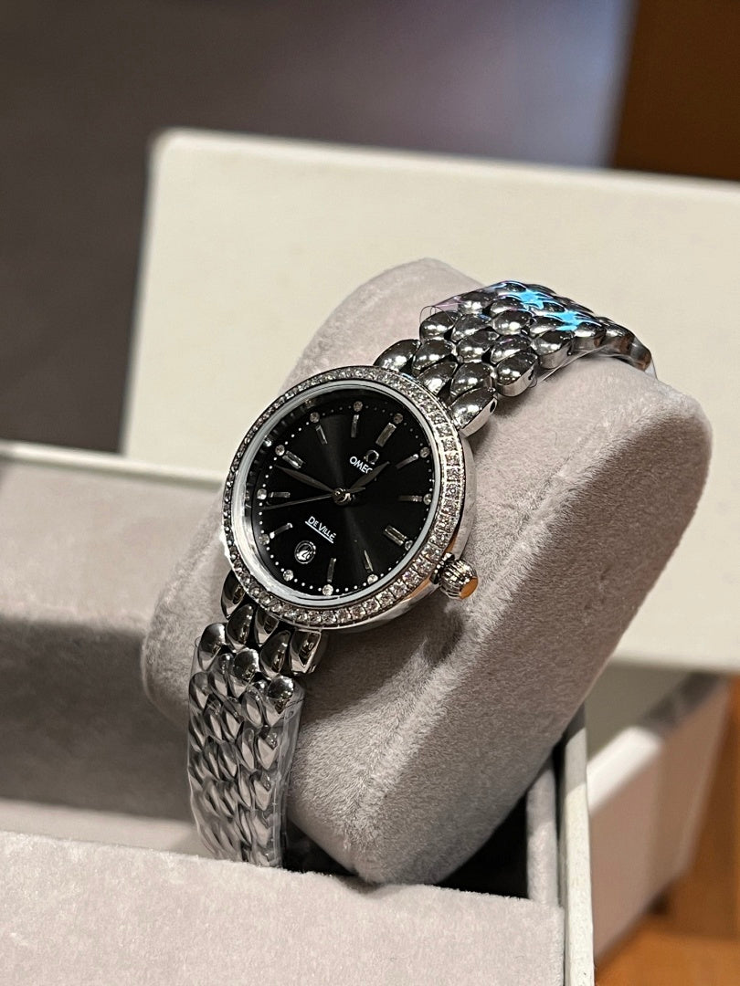 Omega wristwatch with black dial, jeweled bezel with blue accent, textured silver band