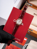 Omega wristwatch, burgundy leather strap with silver dial and bezel, held by black glove