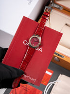 Omega wristwatch with red dial, red leather strap and clasp, held by black glove