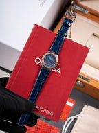 Omega wristwatch with blue dial, blue leather strap and clasp, held by black glove