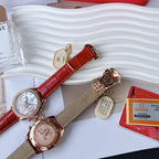 Two round-face wristwatches with red leather straps and gold-toned cases on display