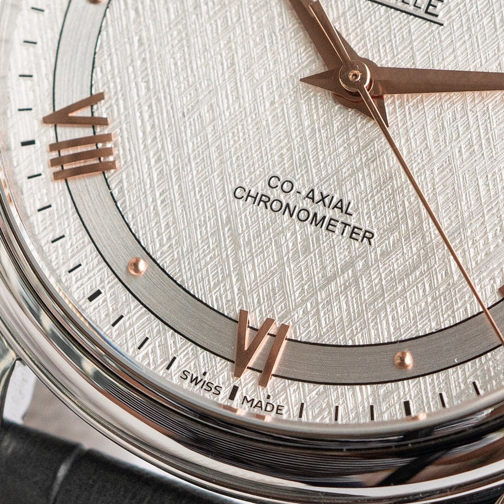 Omega wristwatch dial close-up with rose-gold markers, CO-AXIAL text, date markers