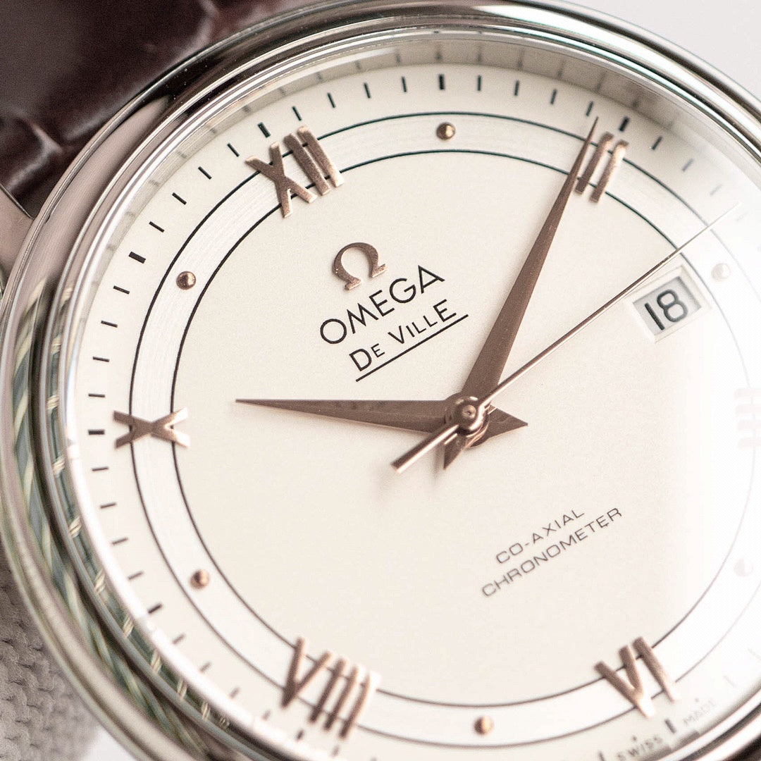 Omega De Ville watch face close-up with white dial, gold markers, hands, date at 18