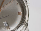 Gray textured watch dial with Roman numerals and gold-tone hour markers