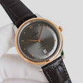 Analog wristwatch, dark gray dial, gold-tone case, black leather strap, day-date window