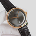 Analog wristwatch, dark gray dial, gold-tone case, black leather strap, day-date window