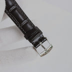 Black leather watch strap with metal buckle on an analog wristwatch