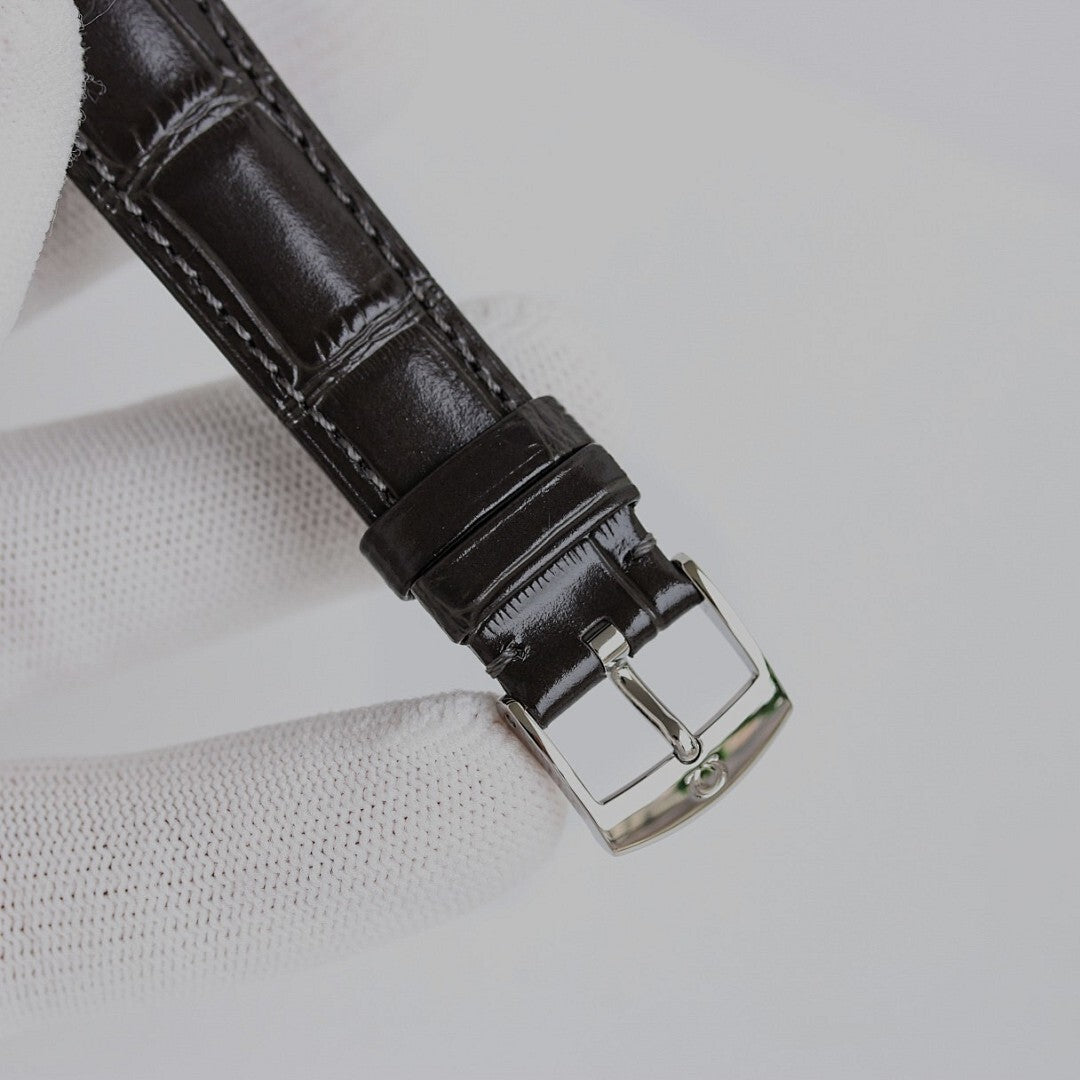 Black leather watch strap with metal buckle on an analog wristwatch