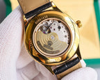 Gold-tone watch case back with visible mechanical movement and black leather strap