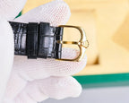 Black leather watch strap with gold-tone buckle and clasp on wristwatch case