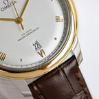 Omega watch closeup: white dial with Roman numerals, date window, brown leather strap.