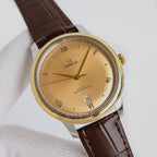Omega watch with gold tone case, beige dial, brown leather strap, roman numerals.