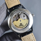 Wristwatch caseback showing mechanical movement and gold balance wheel, black strap