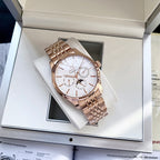 Rose-gold tone wristwatch on a white cushion inside a gift box with metal link bracelet.