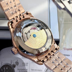 Rose-gold tone wristwatch case close-up with see-through back and metal link bracelet.