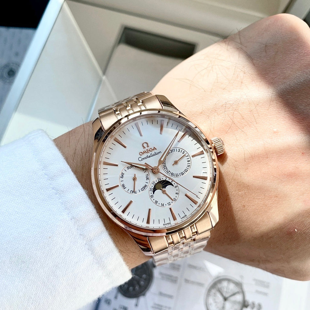 Rose-gold tone wristwatch with white dial and metal link bracelet worn on a hand.