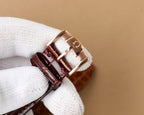 Omega wristwatch with rose-gold buckle and brown leather strap on white glove